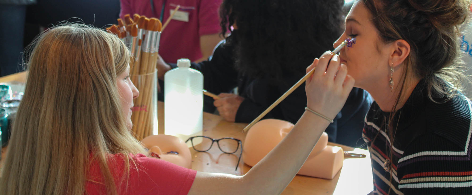 a child painting the face of a woman