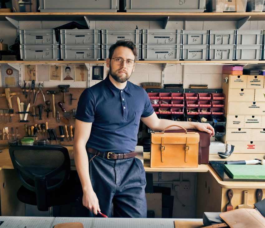 man in a workshop with his arm on a leather bag