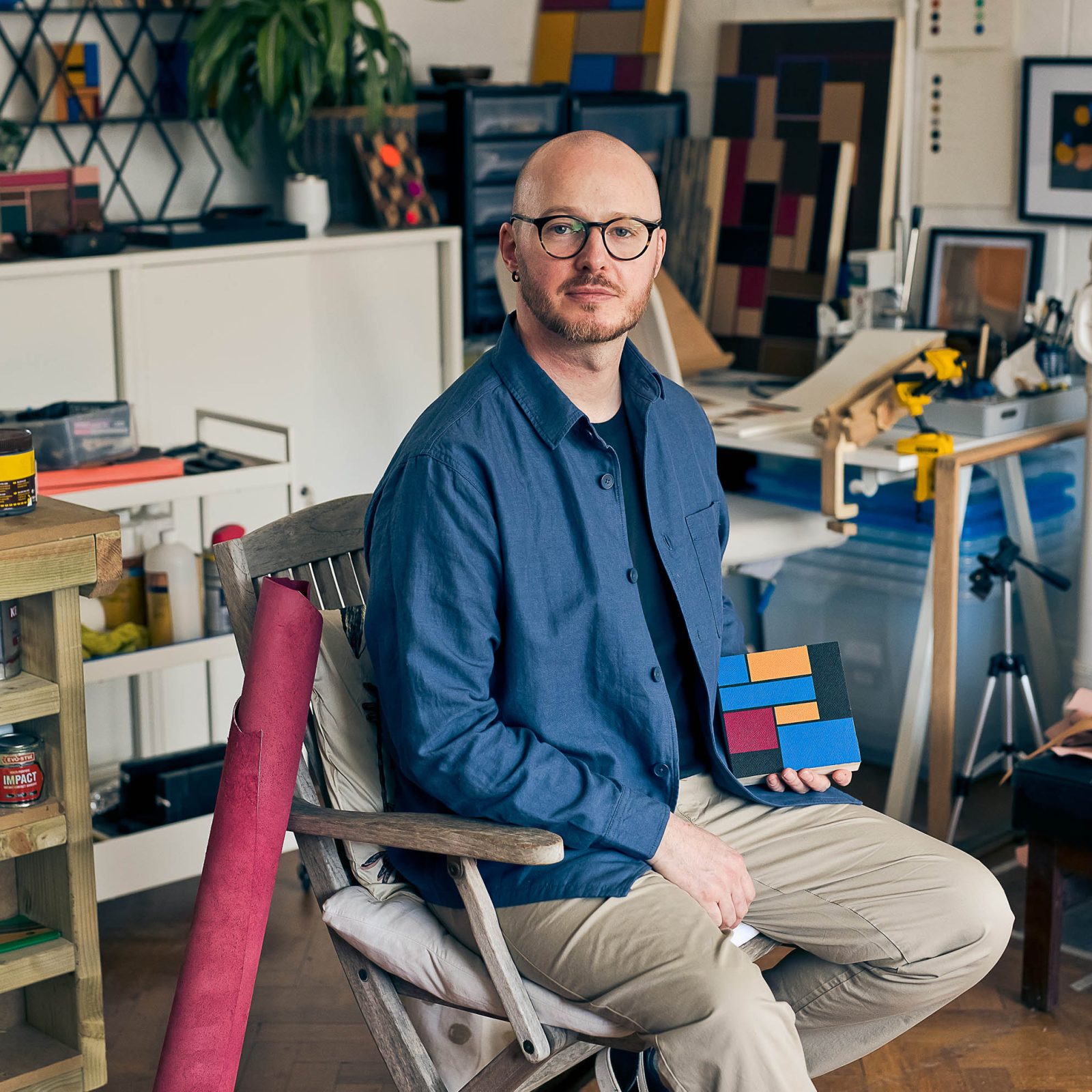 Man on chair holding a square leather pattern in a workshop