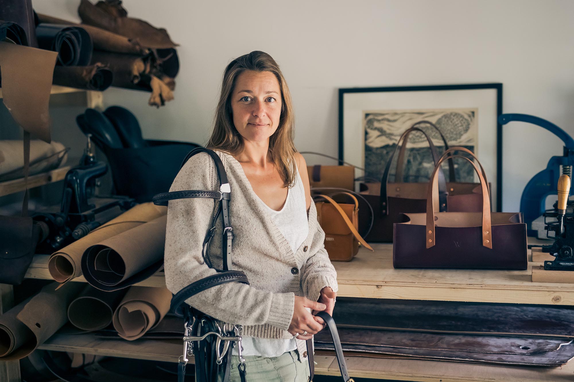 woman holding leather accessories with bags in the background