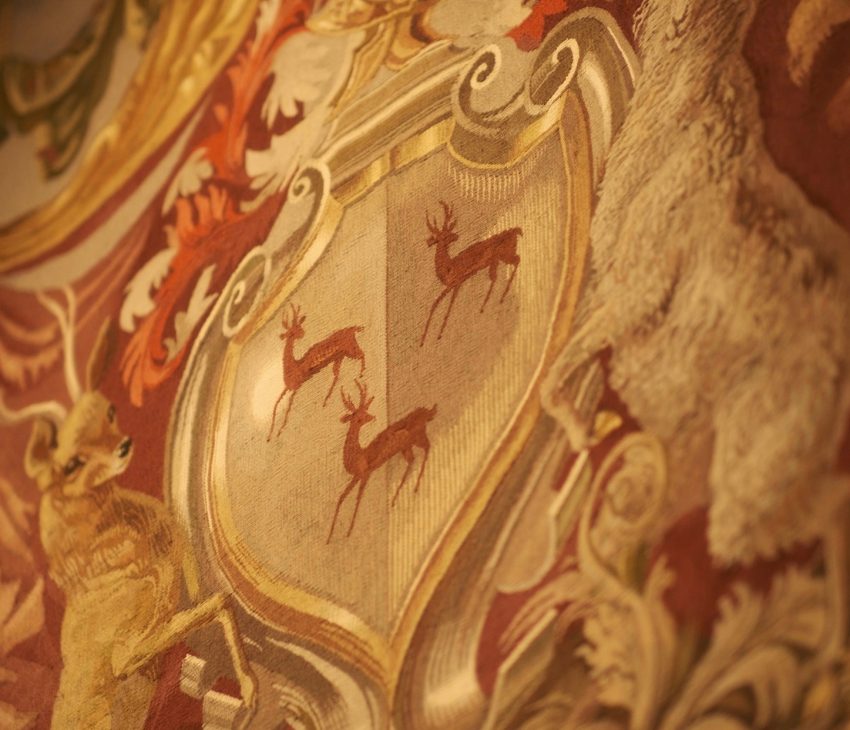 A tapestry of a heraldic achievement with three roebucks inside a shield and a ram and roebuck as supporters.