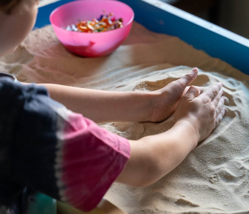 boy playing in a sandpit making patterns with his hands