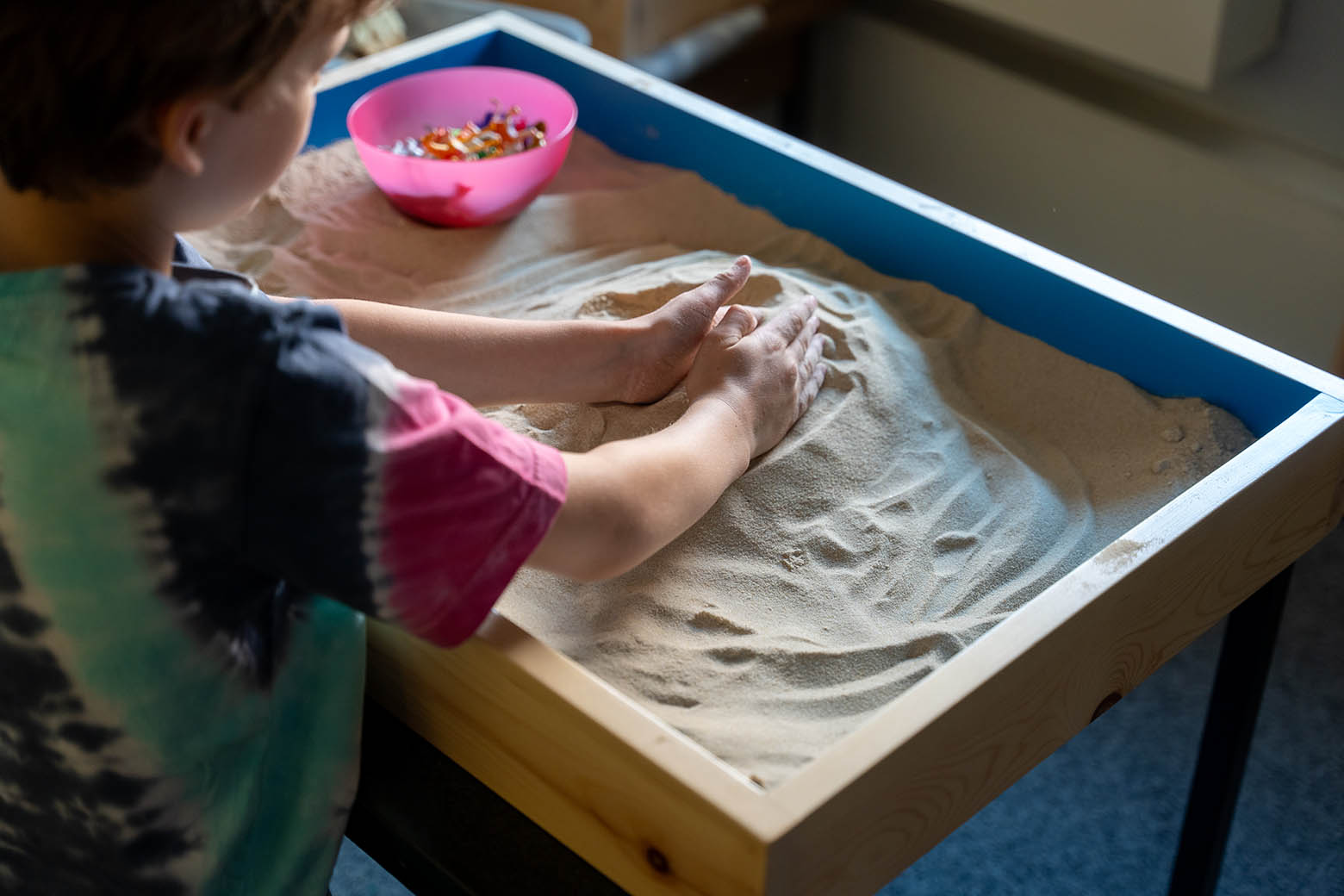 Boy playing in an indoors sandpit, scooping sand with his hands