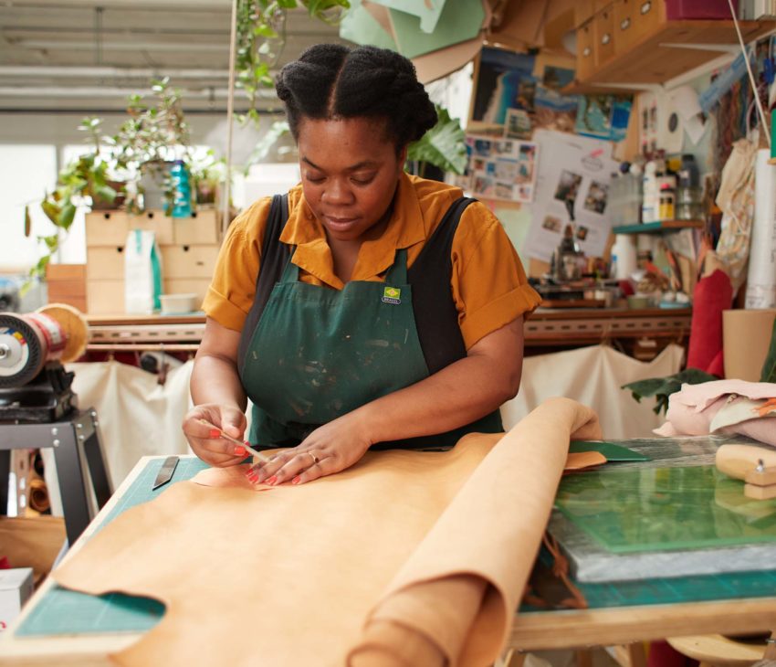 woman in a green apron working with leather in a studio