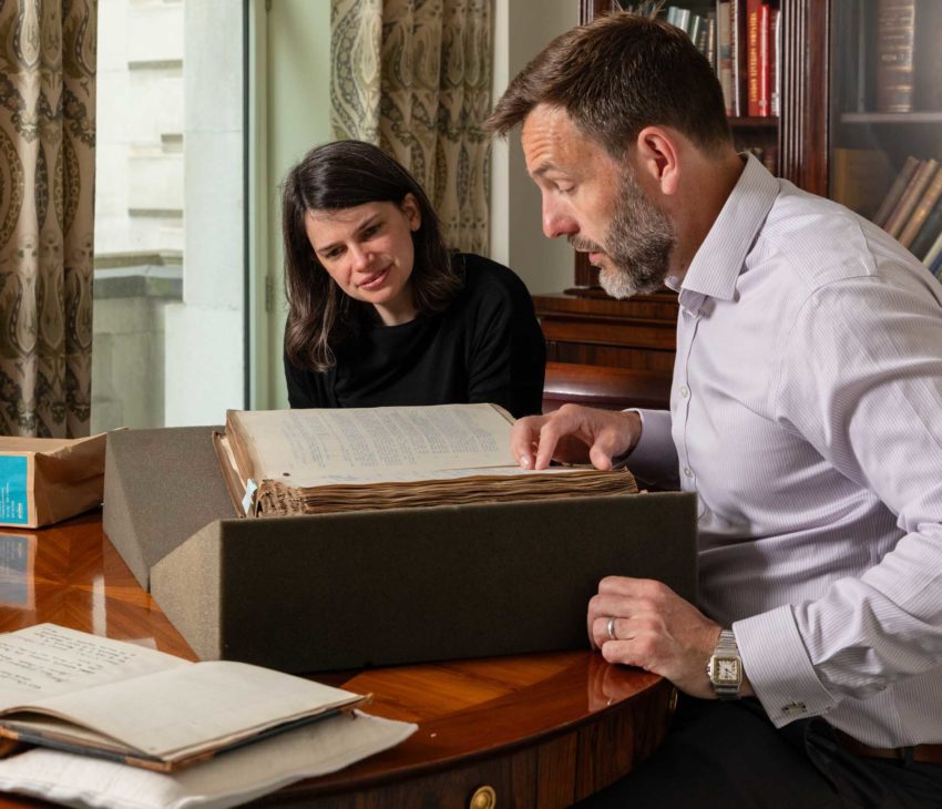 man and a woman sitting at table looking at an old book