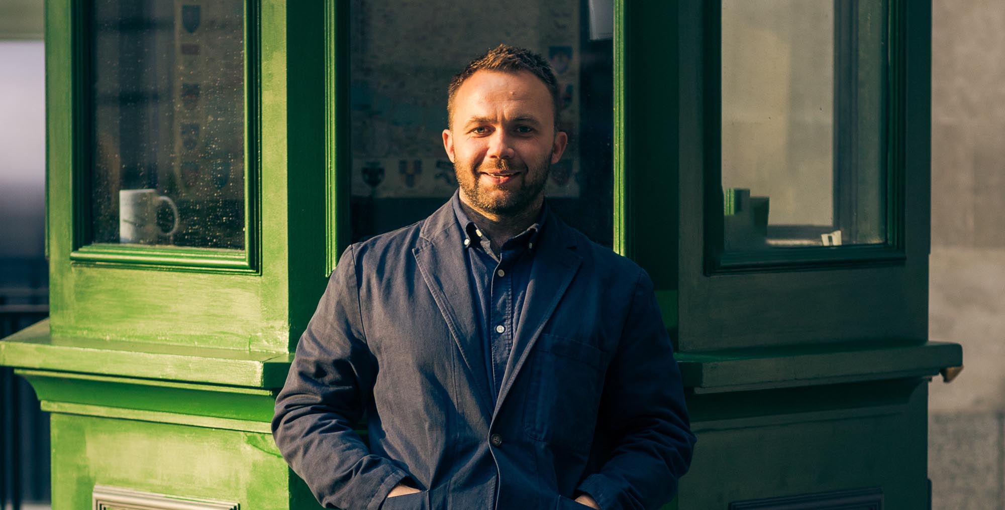 man in a blue coat standing in front of a green hut