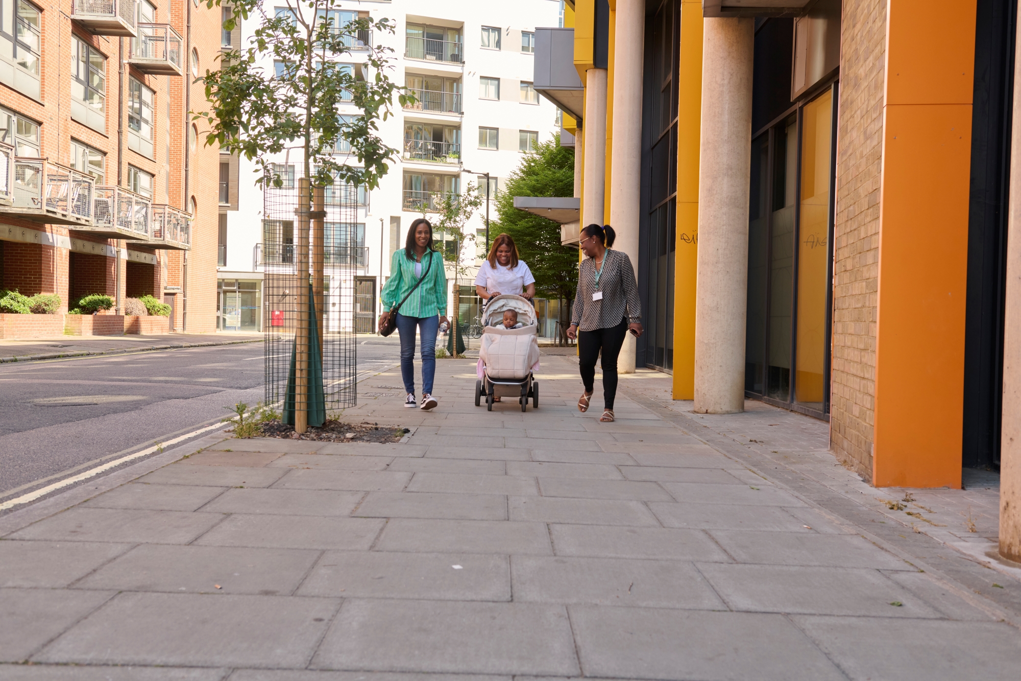 three people push a pram down the street