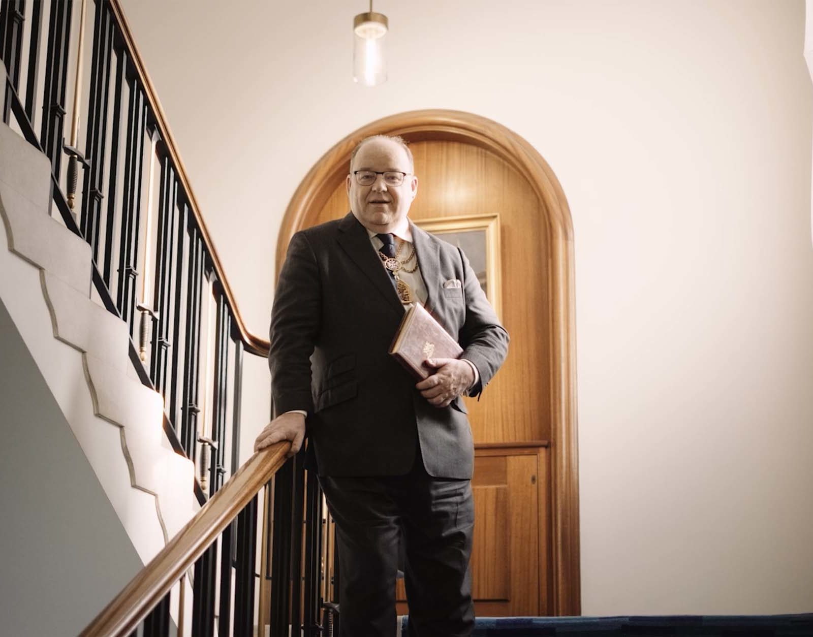 man in suit standing on stairs holding a folder