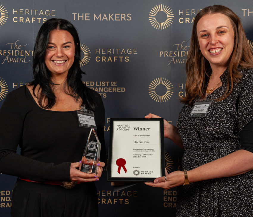 a woman in black holds a glass trophy, while another woman presents a framed certificate
