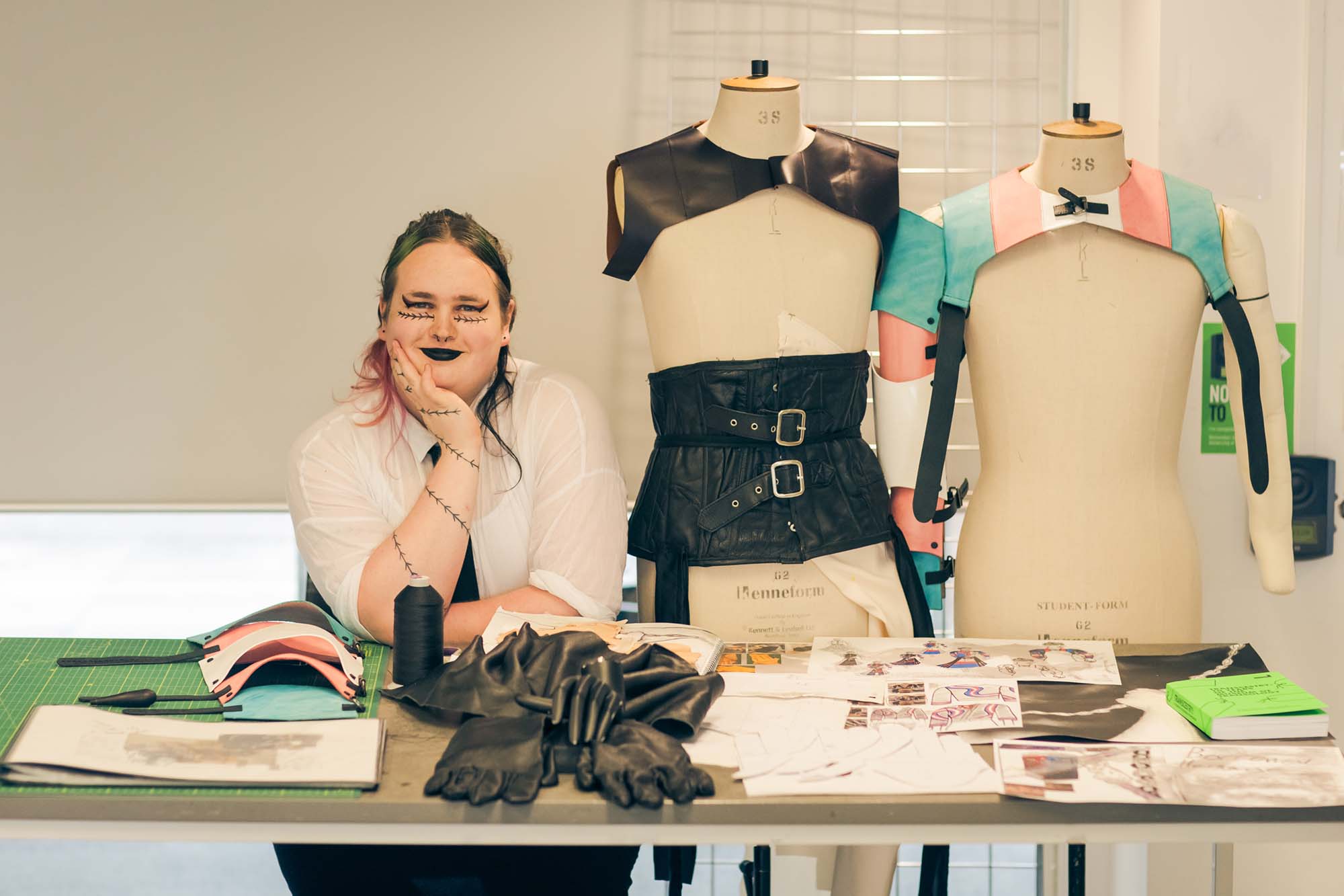 student stands next to two mannequins with leather armor on them.