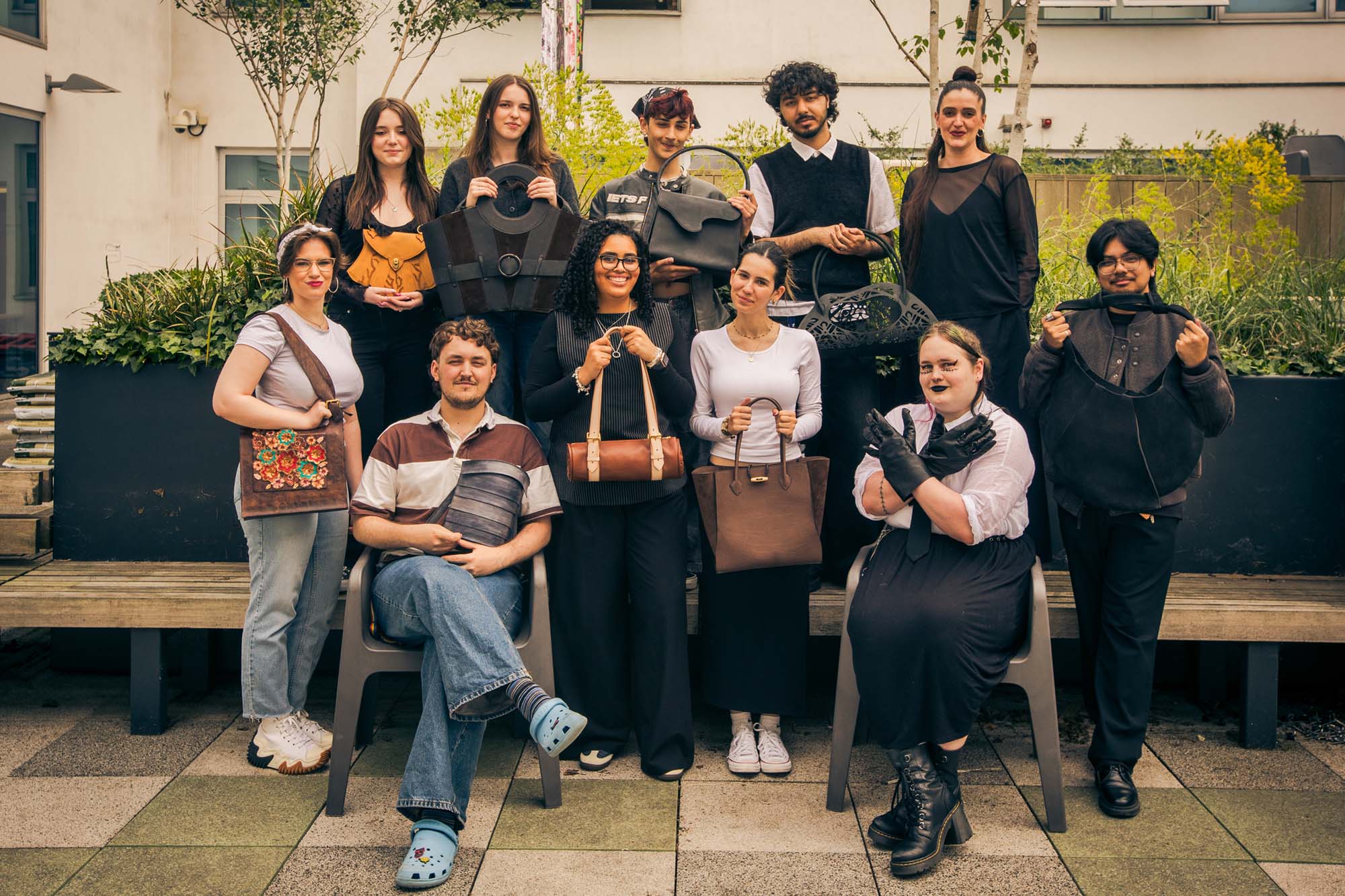 11 students stand outside presenting leather bags