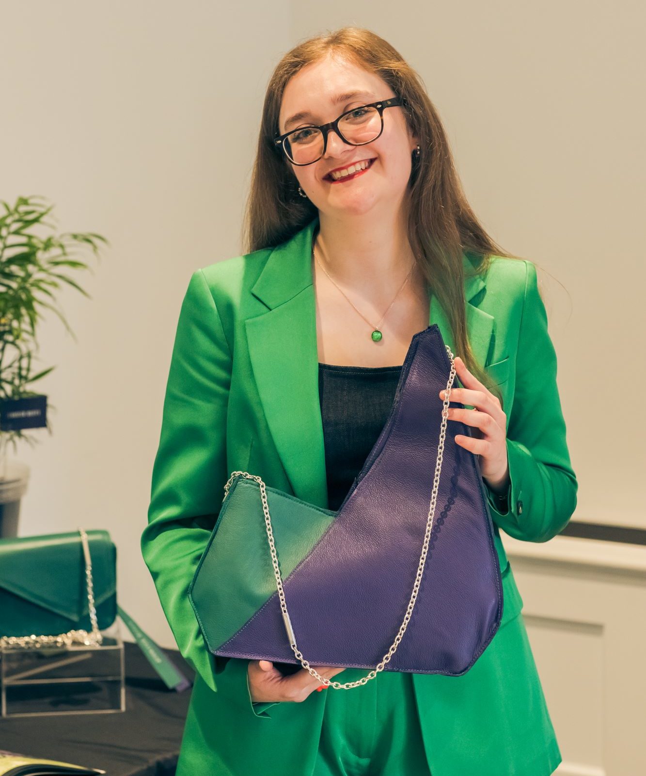 student stands holding a green and purple leather bag