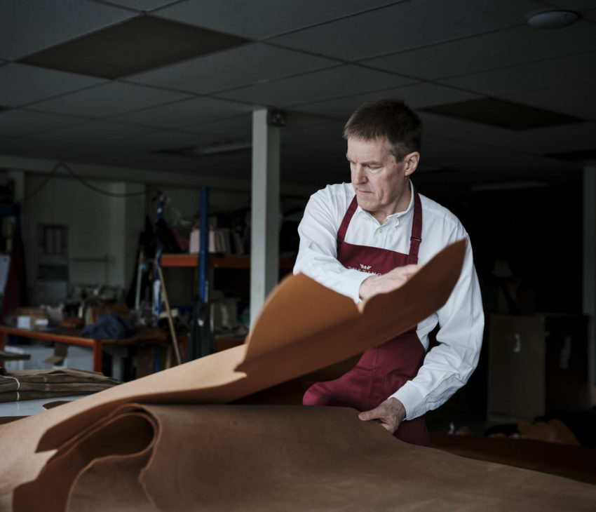 man in an apron spreading a leather hide onto a table