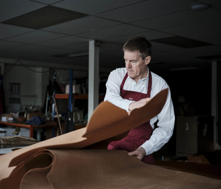 man in an apron spreading a leather hide onto a table