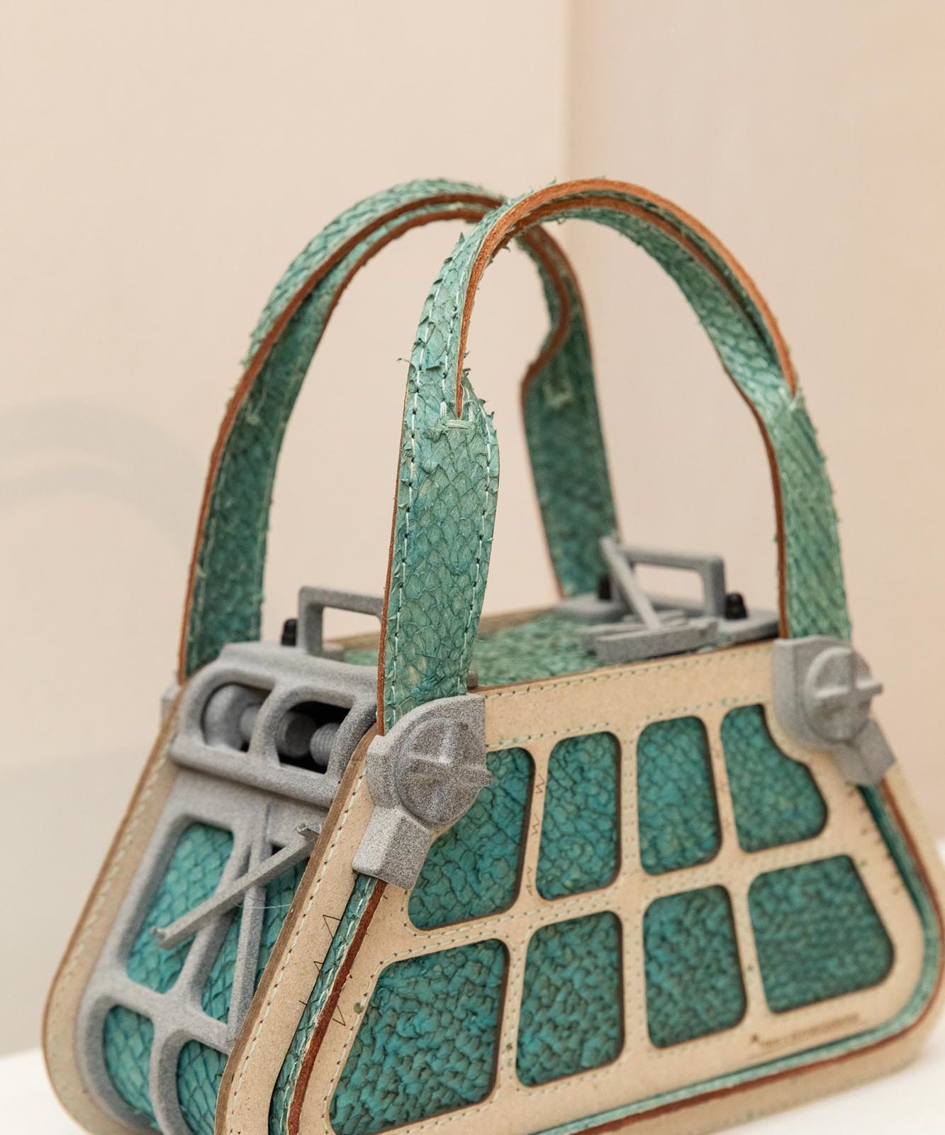 A handbag with teal textured panels, beige trim, and two handles made from fish skin leather.