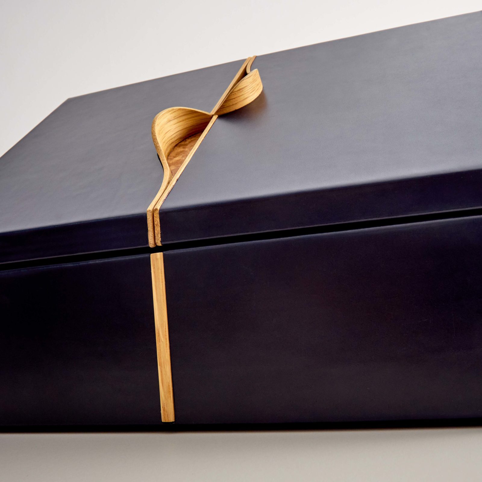 A large, rectangular, black leather box with a distinctive wooden accent running along the centre and up over the top, set against a plain white background.
