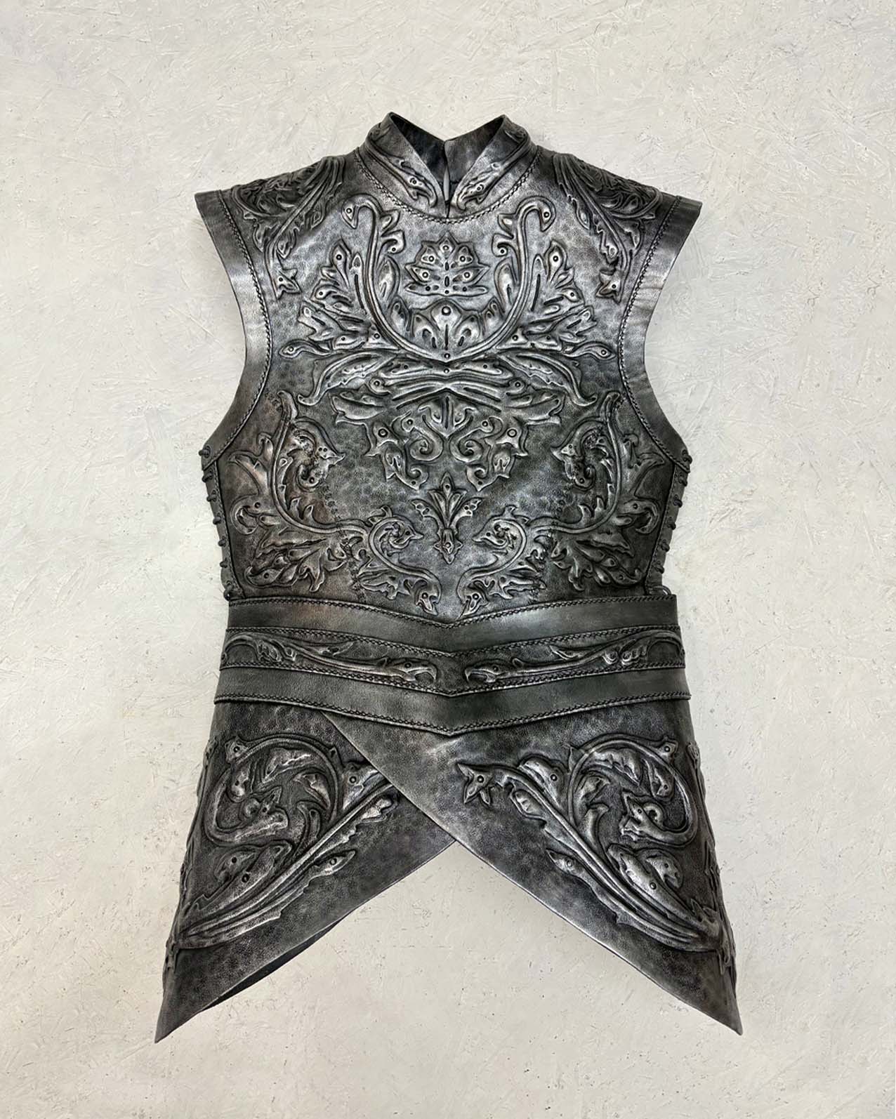 A detailed, ornate leather breastplate armour with raised floral and vine designs, featuring overlapping segments at the waist, displayed flat against a neutral background.